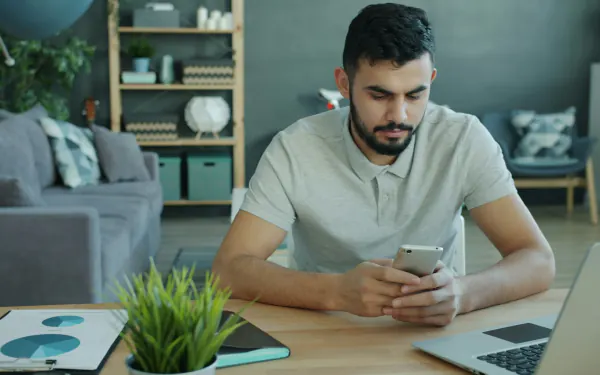 A host checking a phone at a desk with a laptop